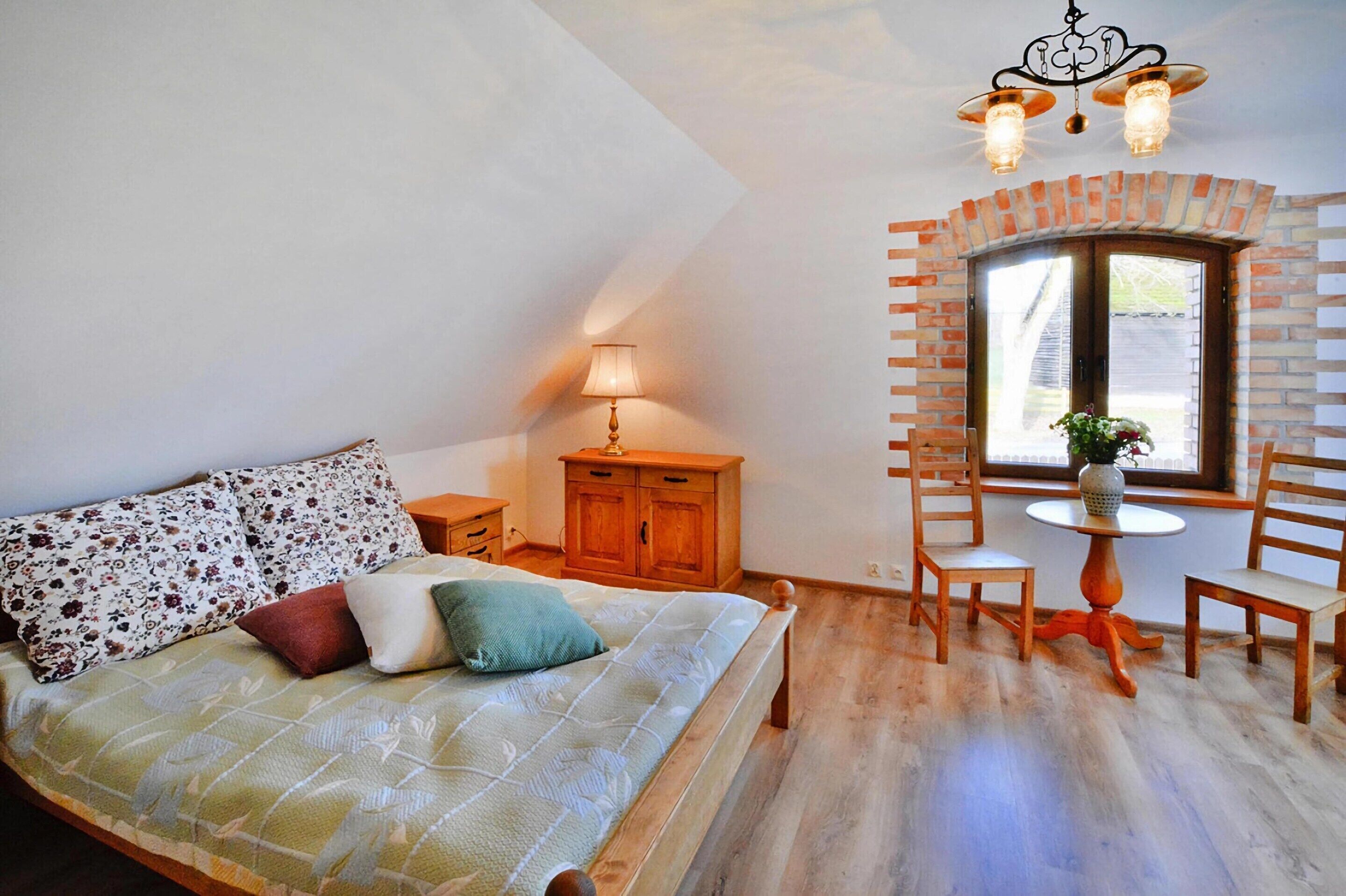 A bedroom with a bed, a nightstand, a lamp, a wooden cabinet, and a window with a view.