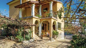 Ένα διώροφο κτίριο με μπαλκόνι, τοξωτά παράθυρα και ένα πλακόστρωτο μονοπάτι που οδηγεί στην είσοδο.