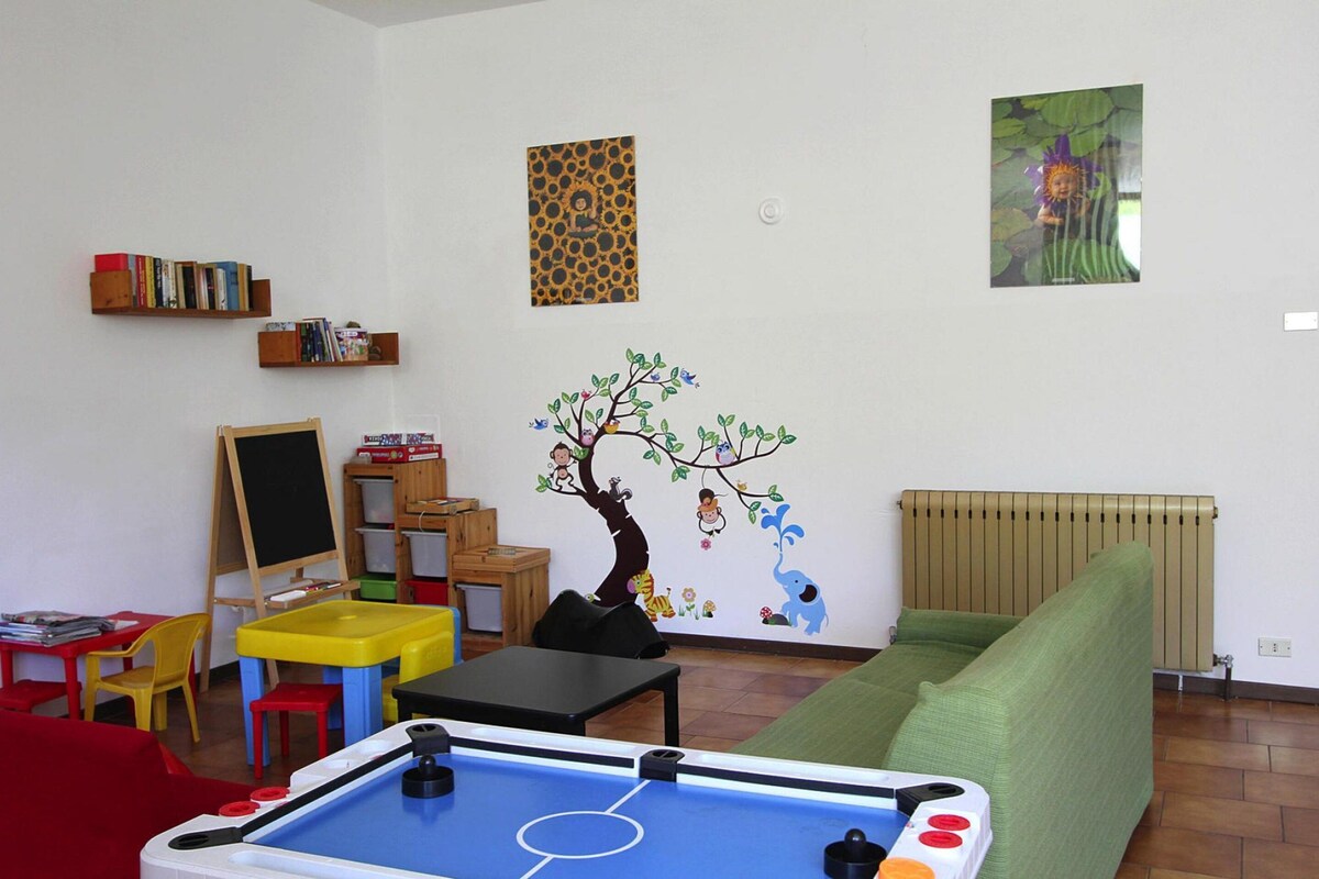 Une salle de jeux pour enfants avec une table de billard, un canapé vert et une fresque représentant un arbre peuplé d’animaux.