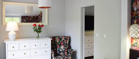 A room with a white dresser, a floral armchair, a small white table, and a hanging light fixture.