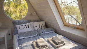 Ein gemütliches Schlafzimmer mit schrägverlaufender Decke, einem Rundfenster und einem Bett mit Kissen, auf denen 'Herr & Frau' steht.