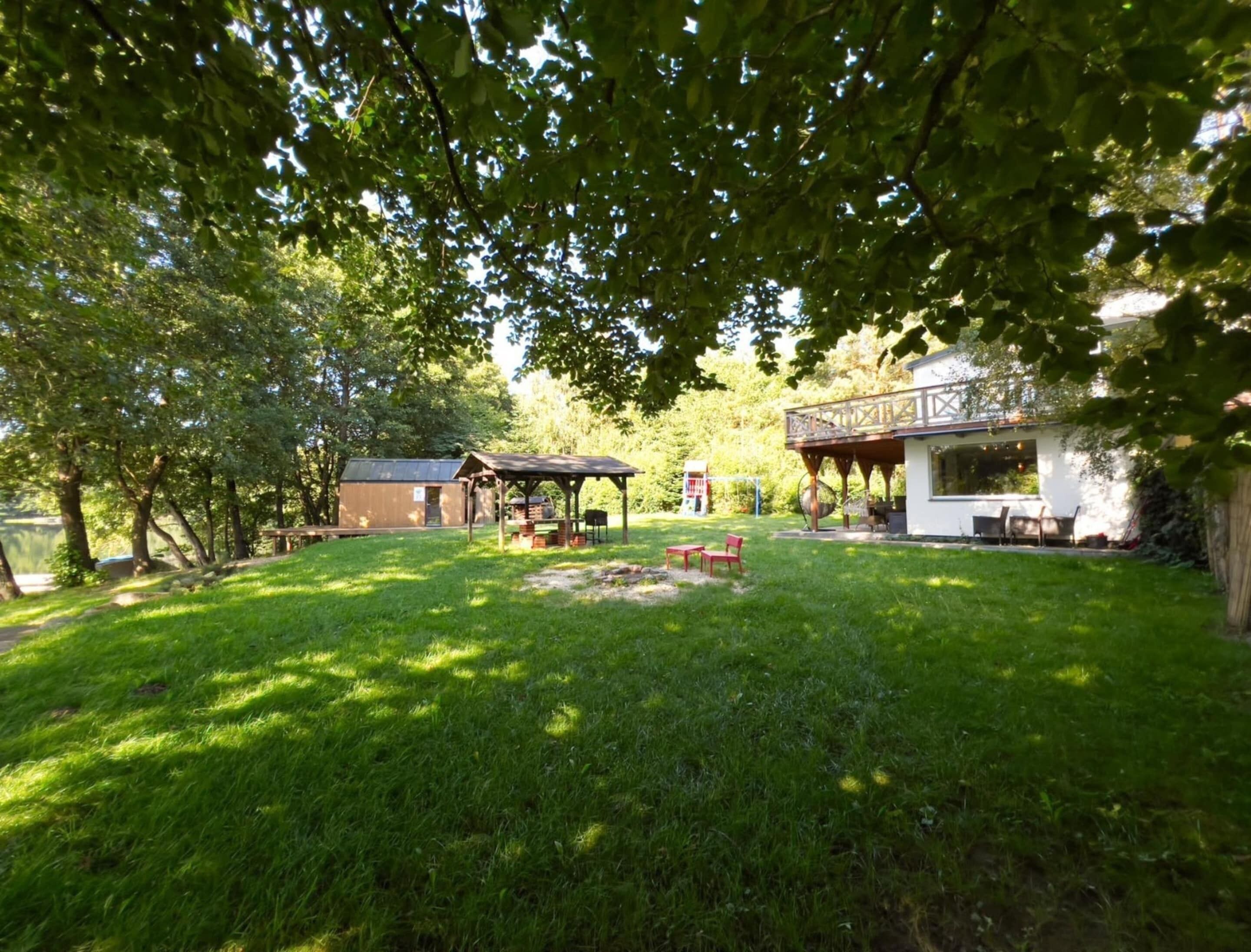 A grassy backyard with a gazebo, a barbecue area, and a building with a balcony.