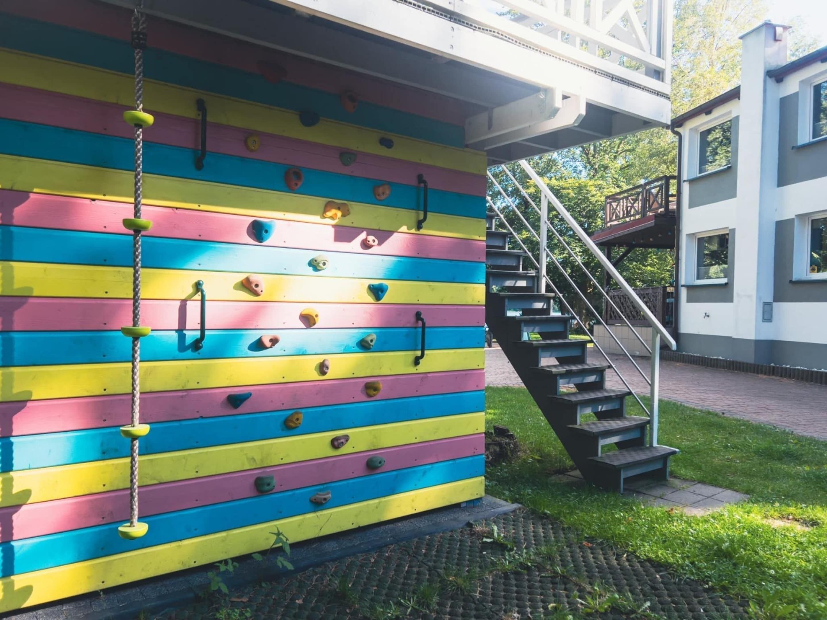 Eine bunte Kletterwand mit einer Treppe, die zu einem Gebäude führt.