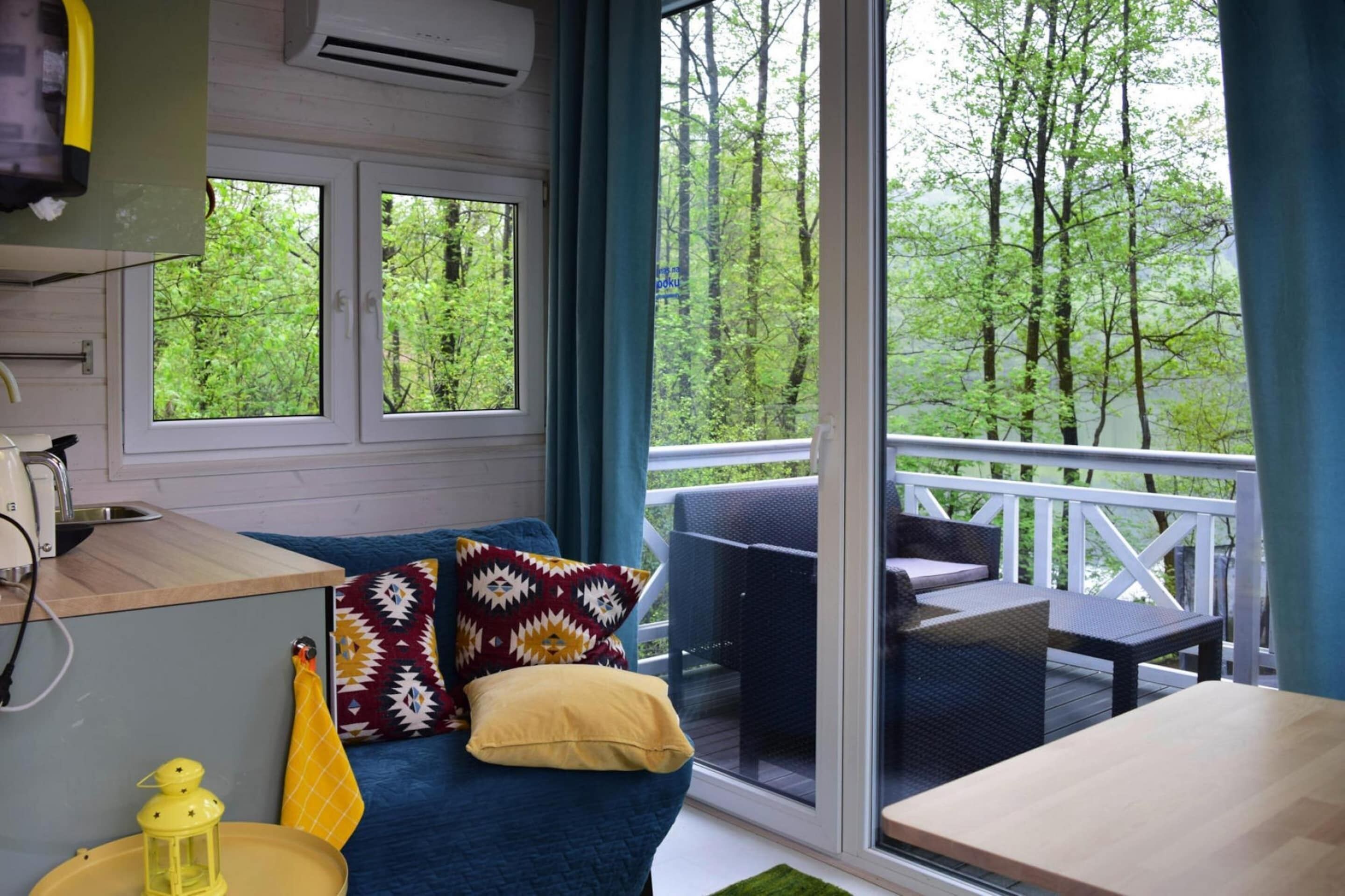 A cozy room with a blue sofa, a small table, and a balcony with a view of trees.