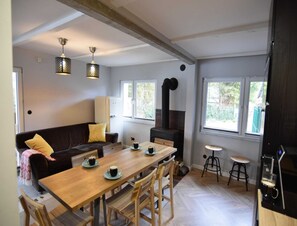 A cozy living area with a sofa, a wooden dining table, and a coffee machine. There is a large window providing natural light and a view of the outdoors. - Semi-detached House Directly on the Lake, Stare Czaple (gmina Stężyca)
