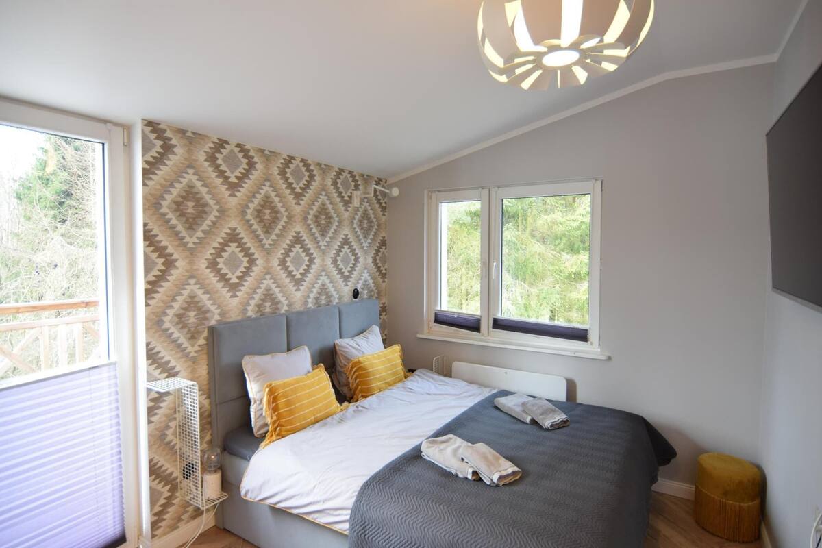 Une chambre à coucher avec un lit, un papier peint à motifs, un luminaire au plafond et des fenêtres.