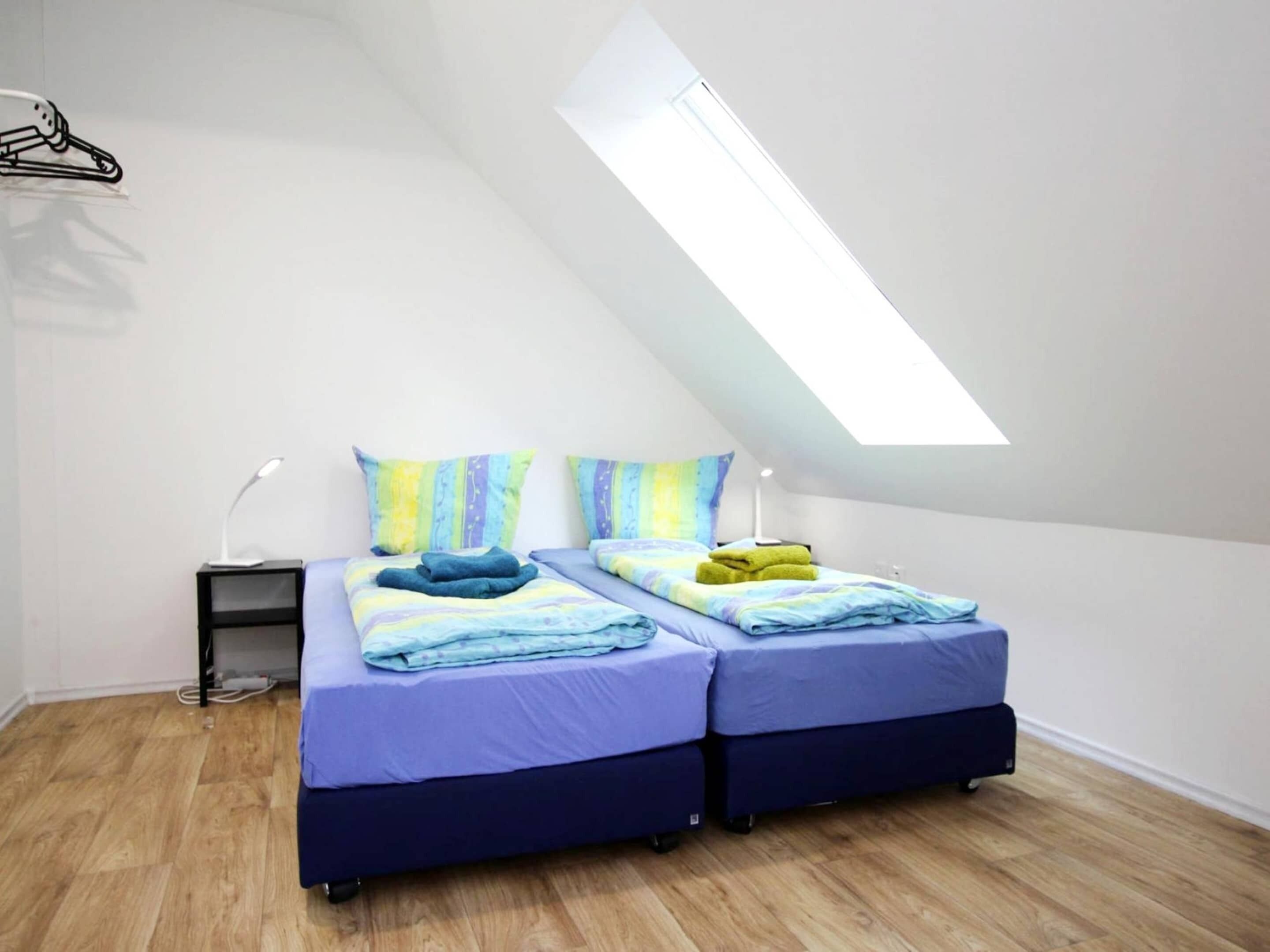 A small, modern bedroom with two beds, a skylight, and a desk with a lamp.