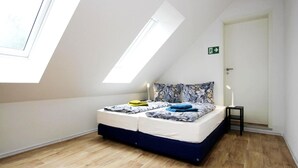 A bedroom with a skylight, a bed with floral bedding, a bedside table with a lamp, and a door with an emergency exit sign.