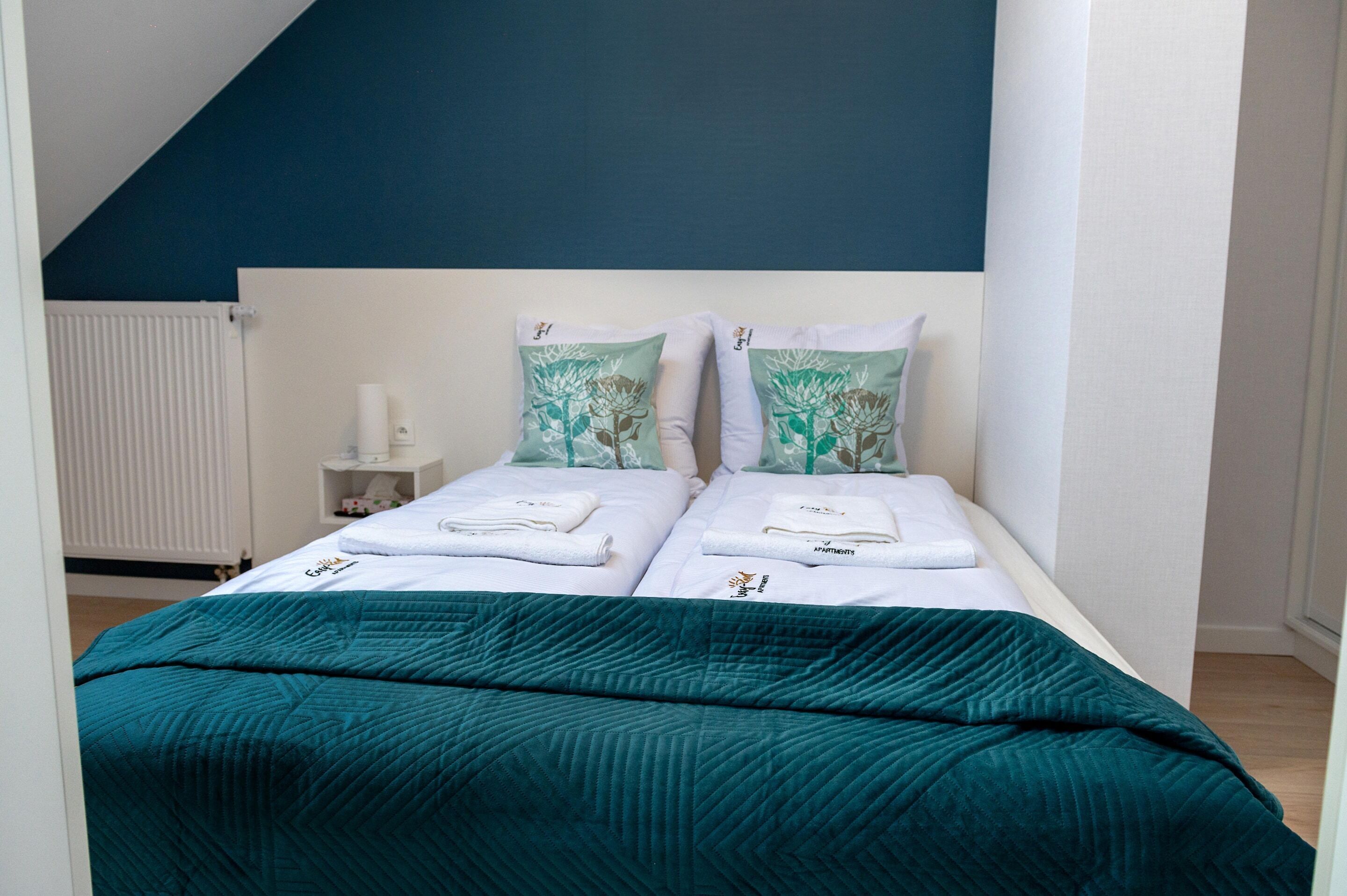A bedroom with two beds, white bedding, teal throw blankets, and matching pillows.