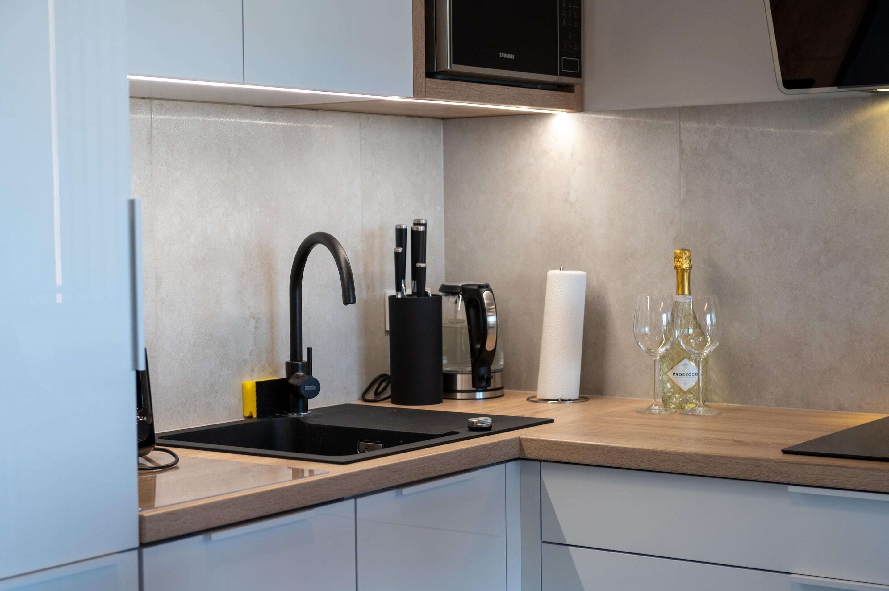 A modern kitchen with a black sink, stainless steel appliances, and a wine bottle on the counter.