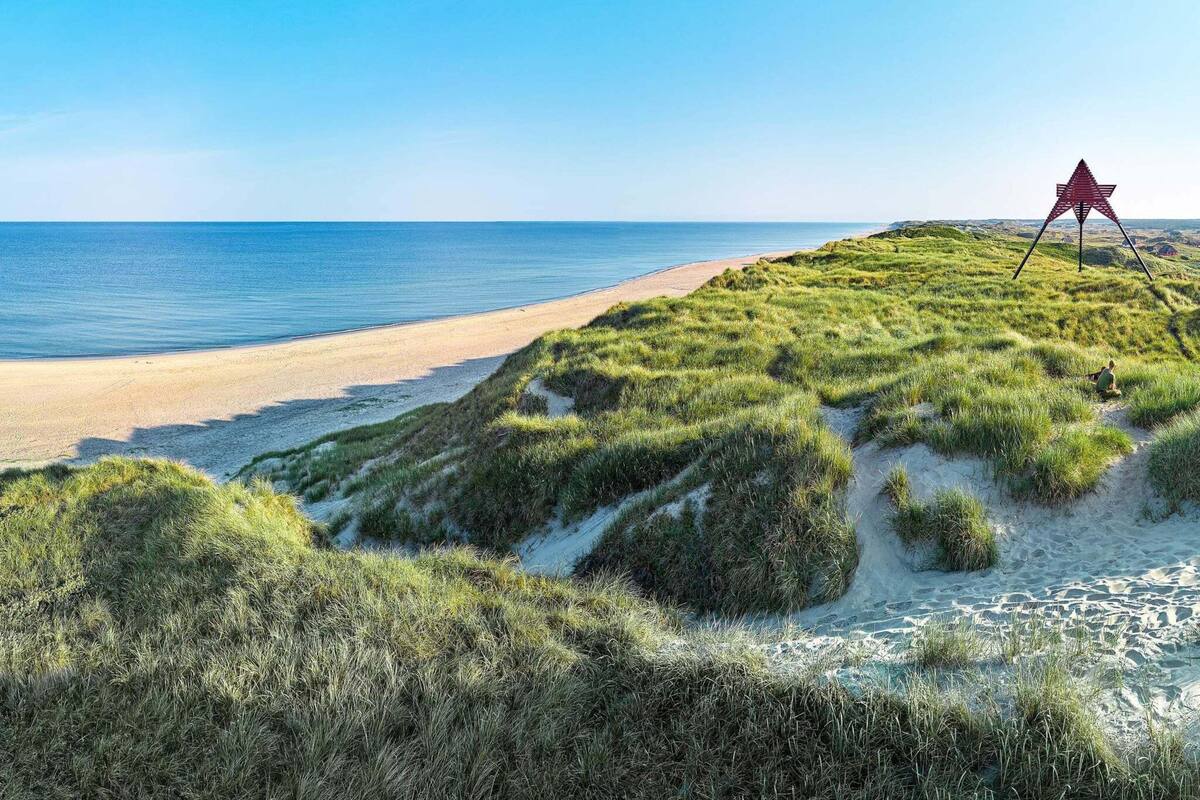 A beach with a dune, a clear sky, and a red structure on the dune.