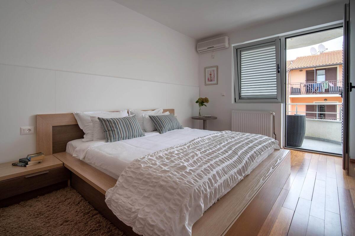 Un dormitorio con cama, mesita de noche y vistas al balcón exterior.
