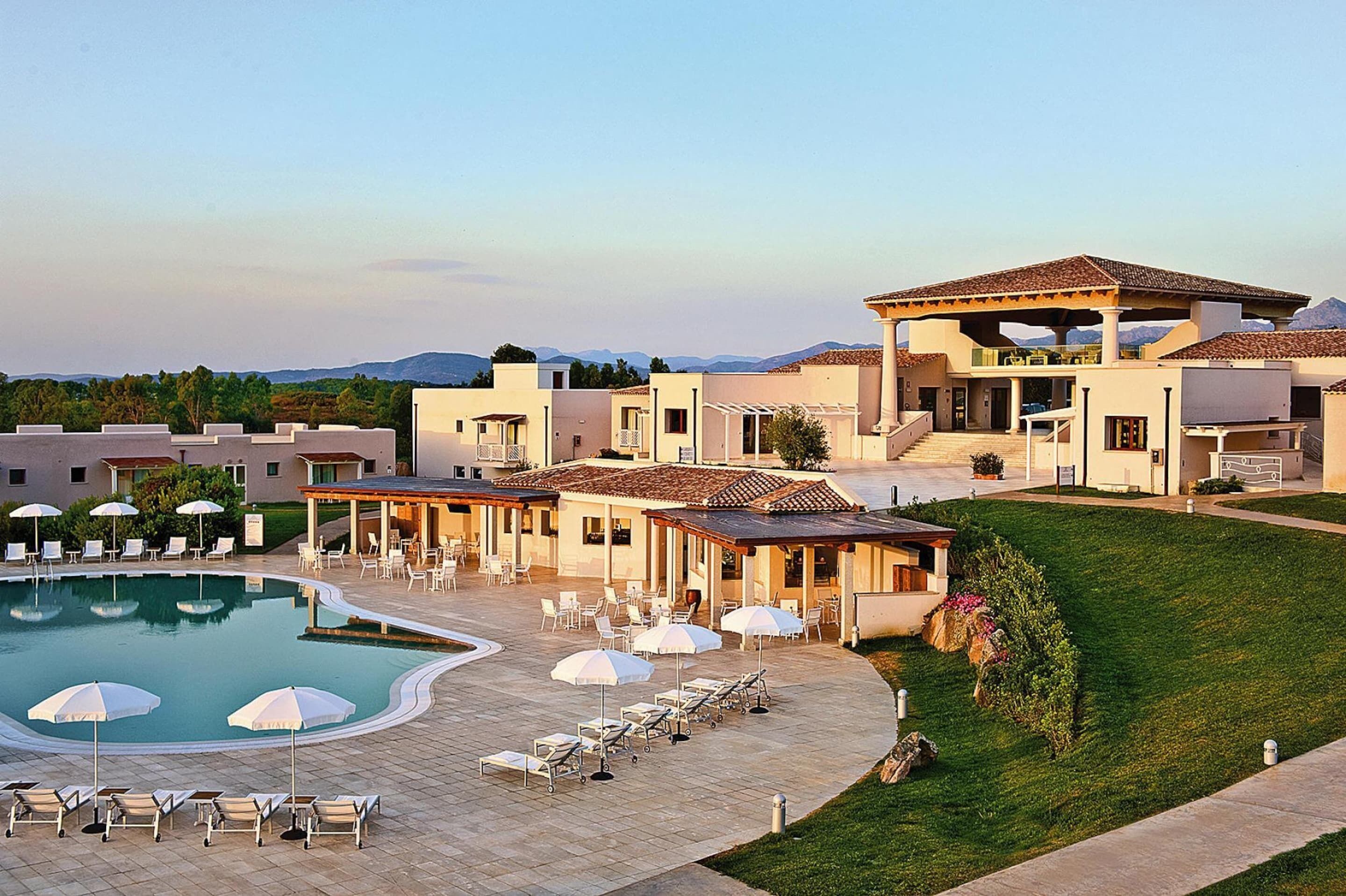 A resort with a swimming pool, lounge chairs, umbrellas, and a covered patio area.