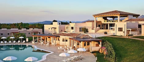 A resort with a swimming pool, lounge chairs, umbrellas, and a covered patio area.