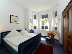 A bedroom with a large bed, a nightstand, a chair, and a wardrobe.