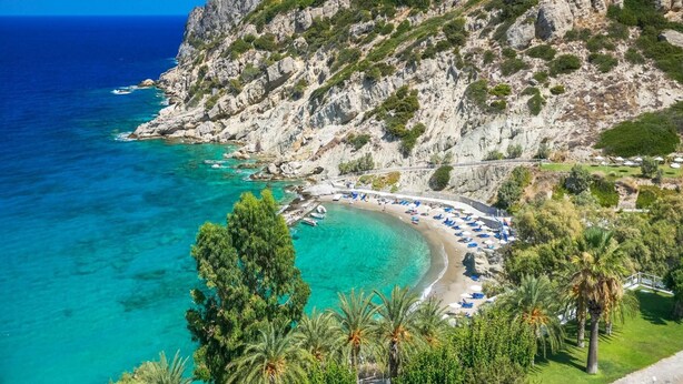 Zona costera con playa, acantilados rocosos y algunos edificios.