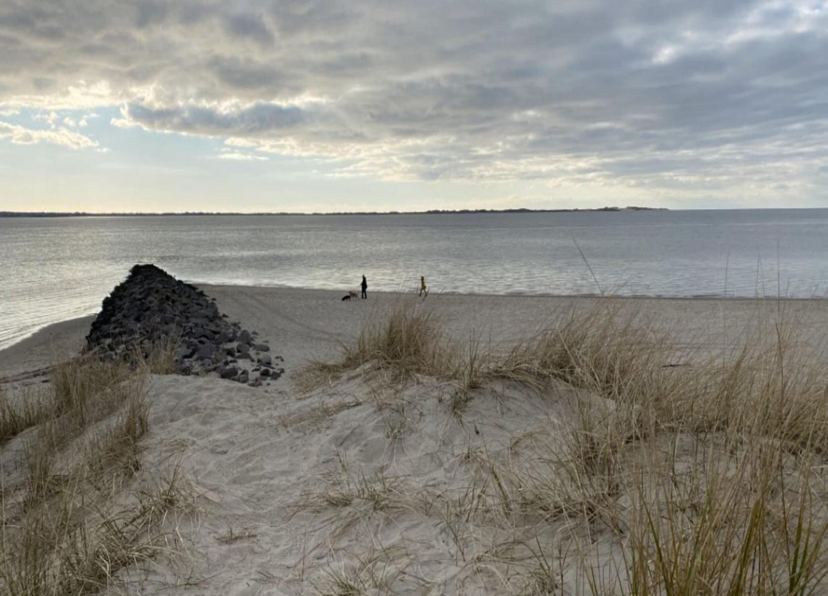 Una playa con dunas de arena y un promontorio rocoso.