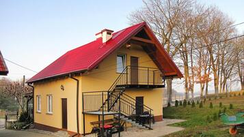 A yellow building with a red roof, a balcony, and a staircase leading to the entrance.