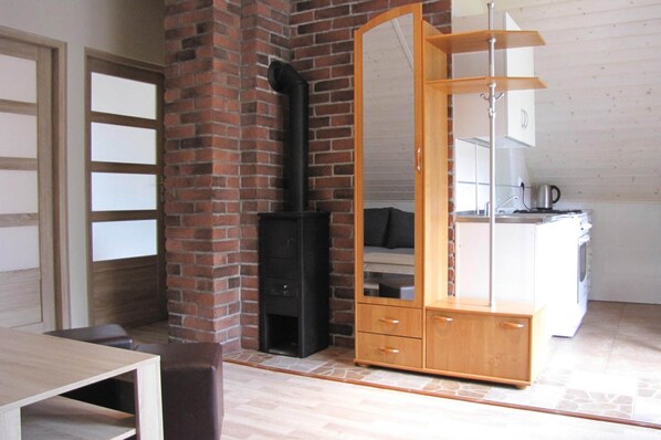 Een kamer met een bakstenen muur, een zwart kachel, een houten kast met lades, een witte wasmachine en een houten tafel.