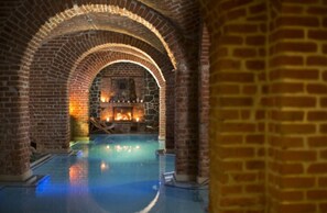An indoor swimming pool with brick arches and a stone fireplace. - Apartment Right on the Lake, Ryn (Ryn)