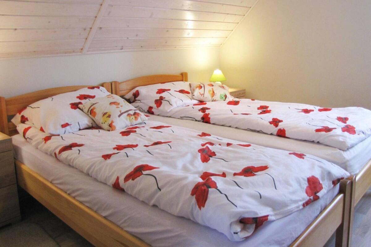 A twin bed with a floral bedspread, a wooden headboard, and a nightstand with a lamp.