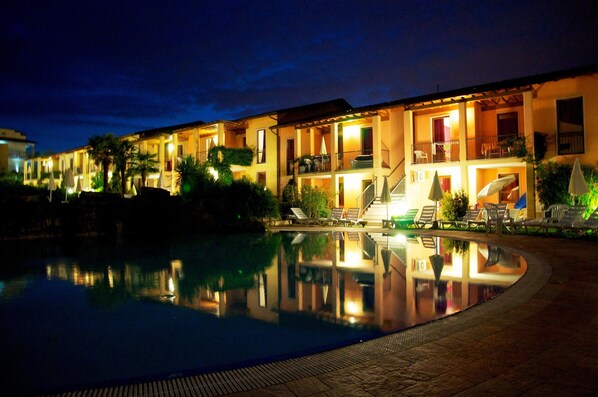 Un hotel con piscina, mobiliario exterior e iluminación destacada en la fachada por la noche.