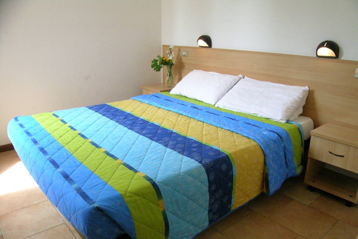 A bed with a quilt, a nightstand, a bedside table, and a wall-mounted lamp.