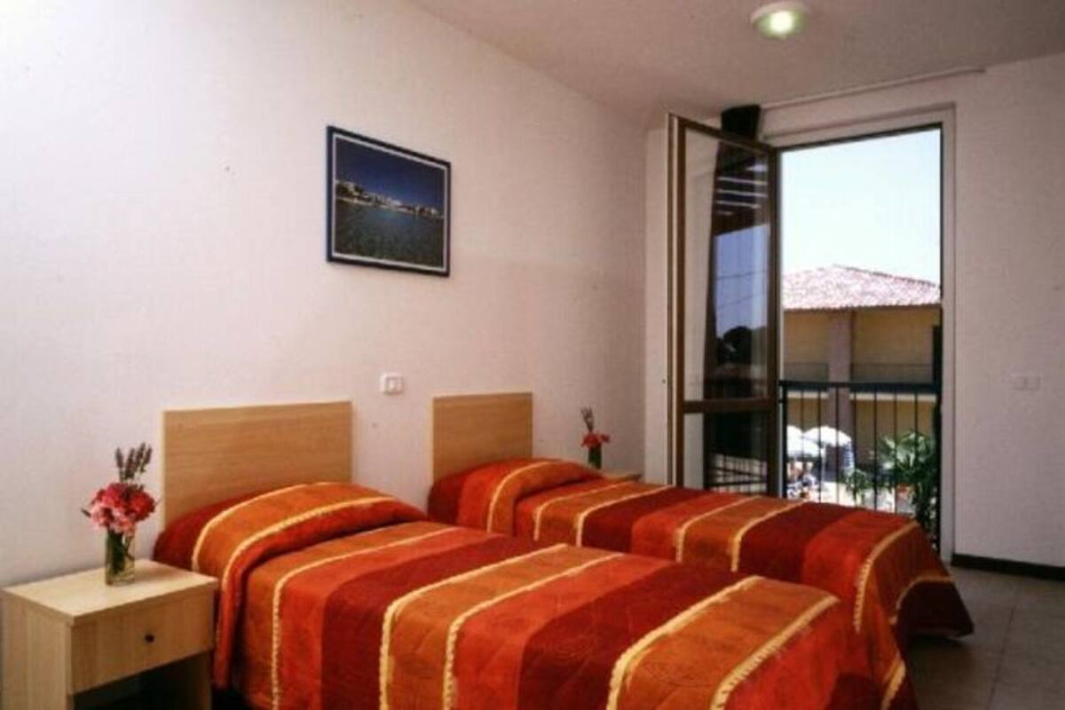 A hotel room with two beds, a nightstand, a vase with flowers, a framed picture on the wall, and a sliding glass door leading to an outdoor area.