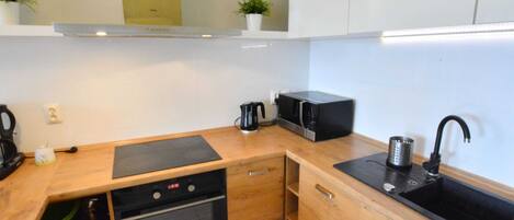 A compact kitchen with wooden cabinets, a built-in oven, a microwave, a coffee maker, and a sink.