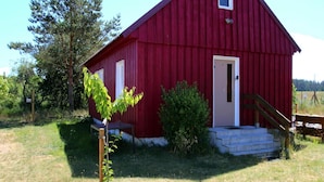 Une grange rouge avec une porte blanche et une petite fenêtre, entourée d’herbe et d’arbres.