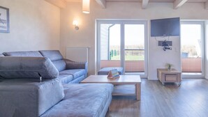 A modern living room with a grey sofa, a wooden coffee table, and a television mounted on the wall. - Exclusively Furnished 5-star Holiday Home Near the Beach (Dagebuell)