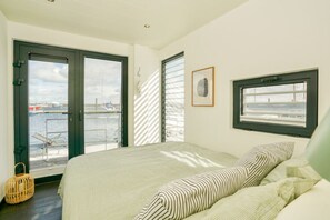 A bedroom with a bed, a window with a view of the water, and a framed picture on the wall. - Houseboat in Boltenhagen (Boltenhagen)