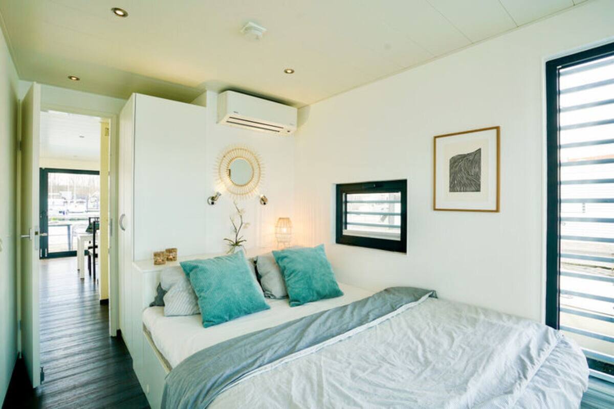 Une chambre à coucher comprenant un lit, une table de chevet, un climatiseur fixé au mur et une fenêtre avec des stores.