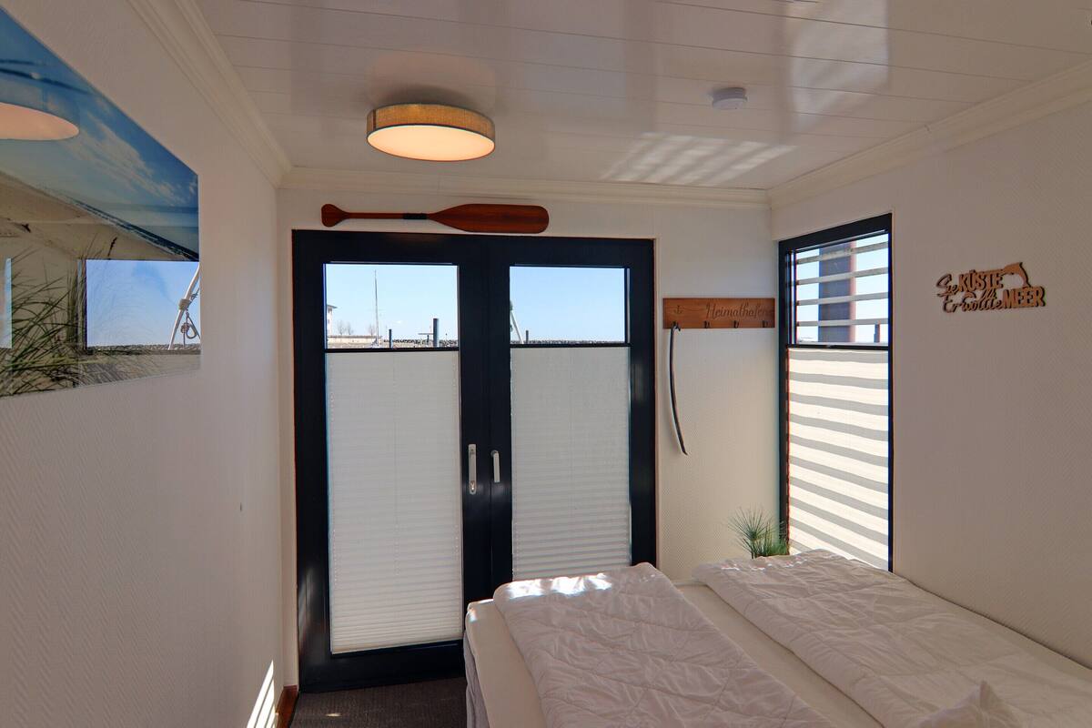 Une chambre d’hôtel avec un lit, une grande fenêtre avec des stores, un luminaire au plafond et un panneau fixé au mur.