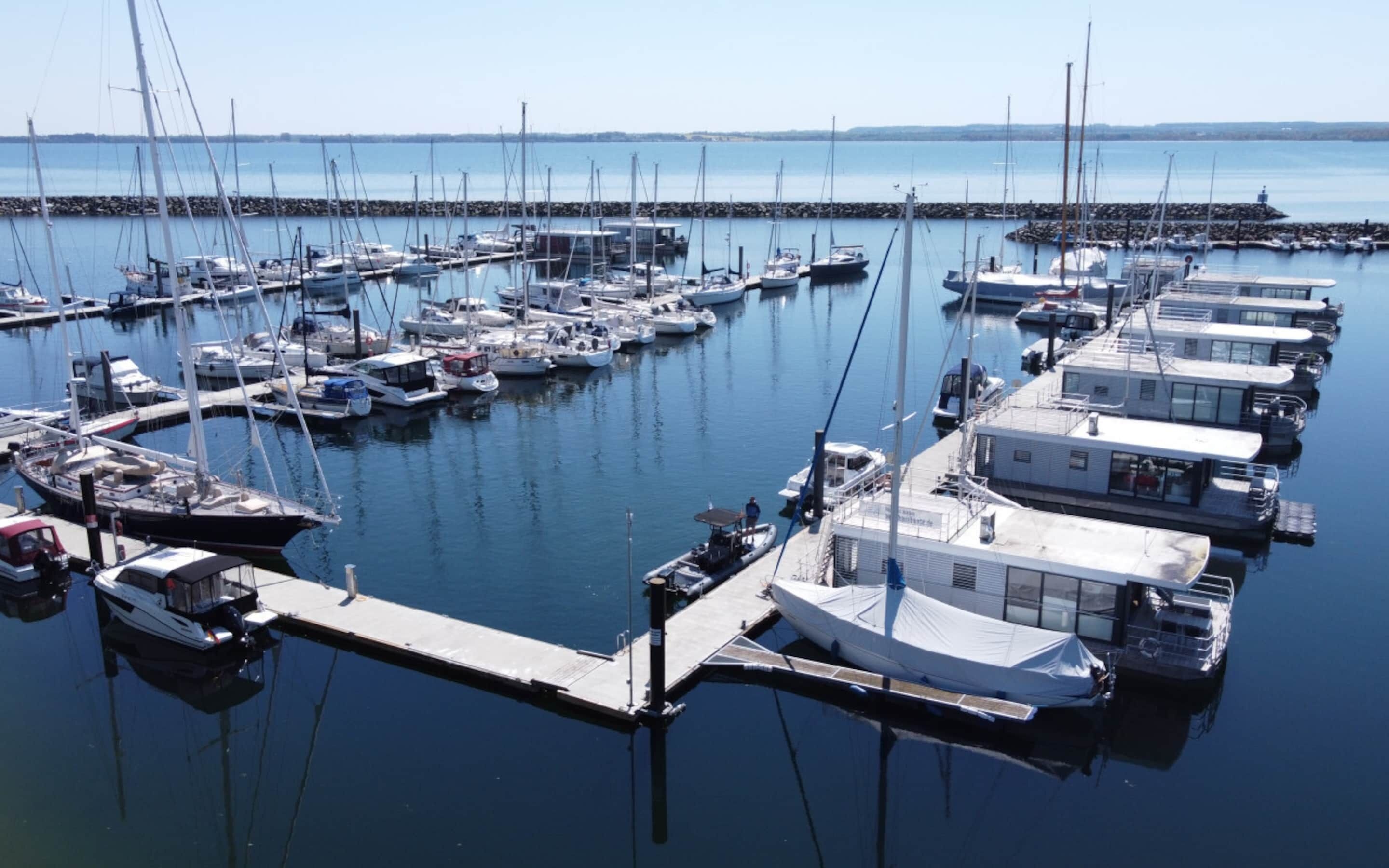 A marina with multiple boats docked at piers, a clear sky, and calm water.