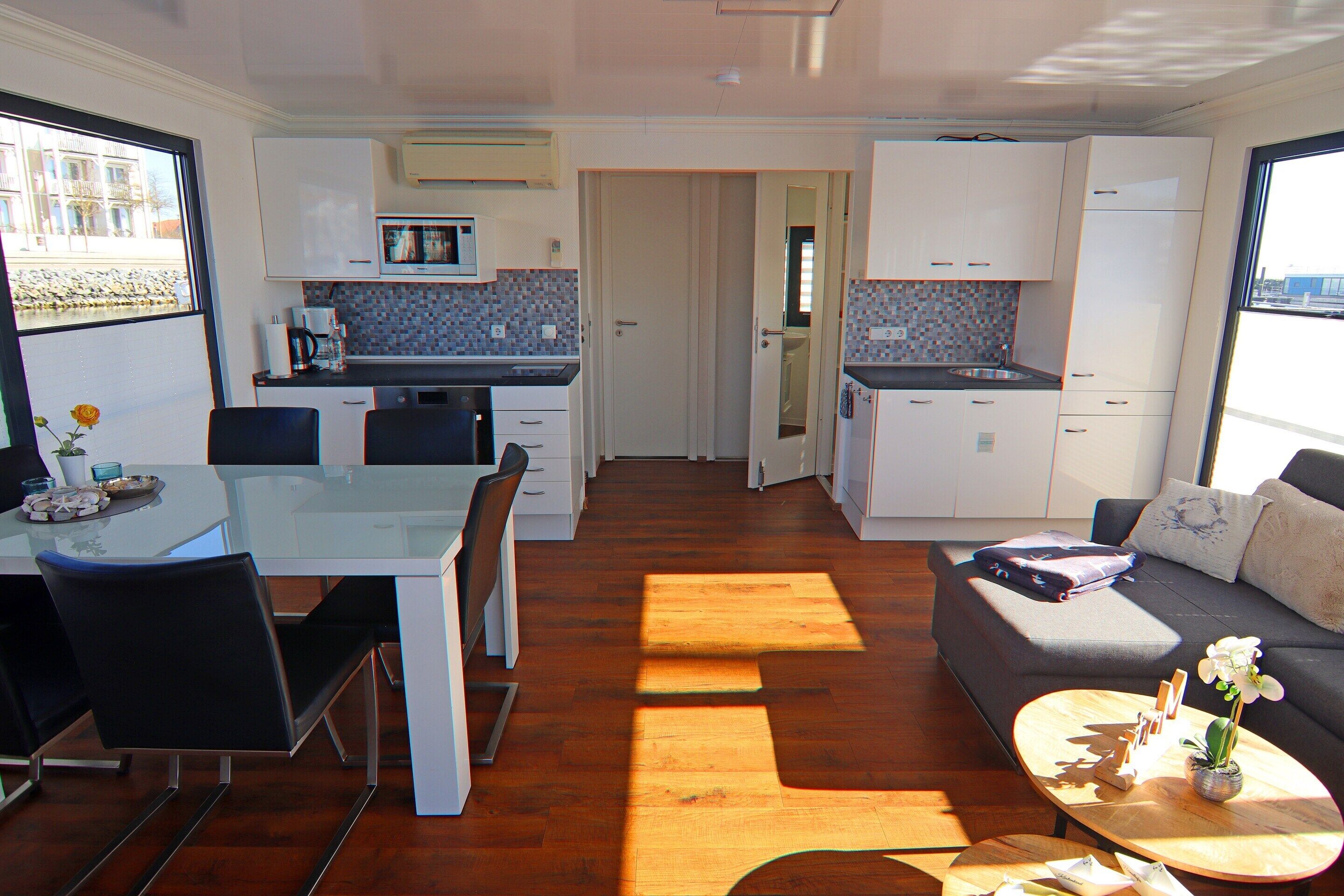 A compact kitchen with modern appliances, a dining area with chairs, and a living space with a sofa and a coffee table.