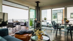 A modern living room with a sofa, a coffee table, and a fireplace. There is a dining area with a table and chairs. The room has large windows with a view of the ocean. - Houseboat in Ribnitz-damgarten (Ribnitz-Damgarten)