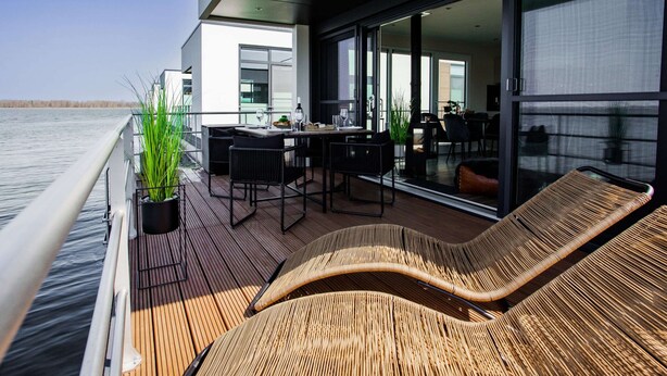 A modern outdoor deck with a dining area, lounge chairs, and a large window overlooking the water. - Houseboat in Ribnitz-damgarten (Ribnitz-Damgarten)