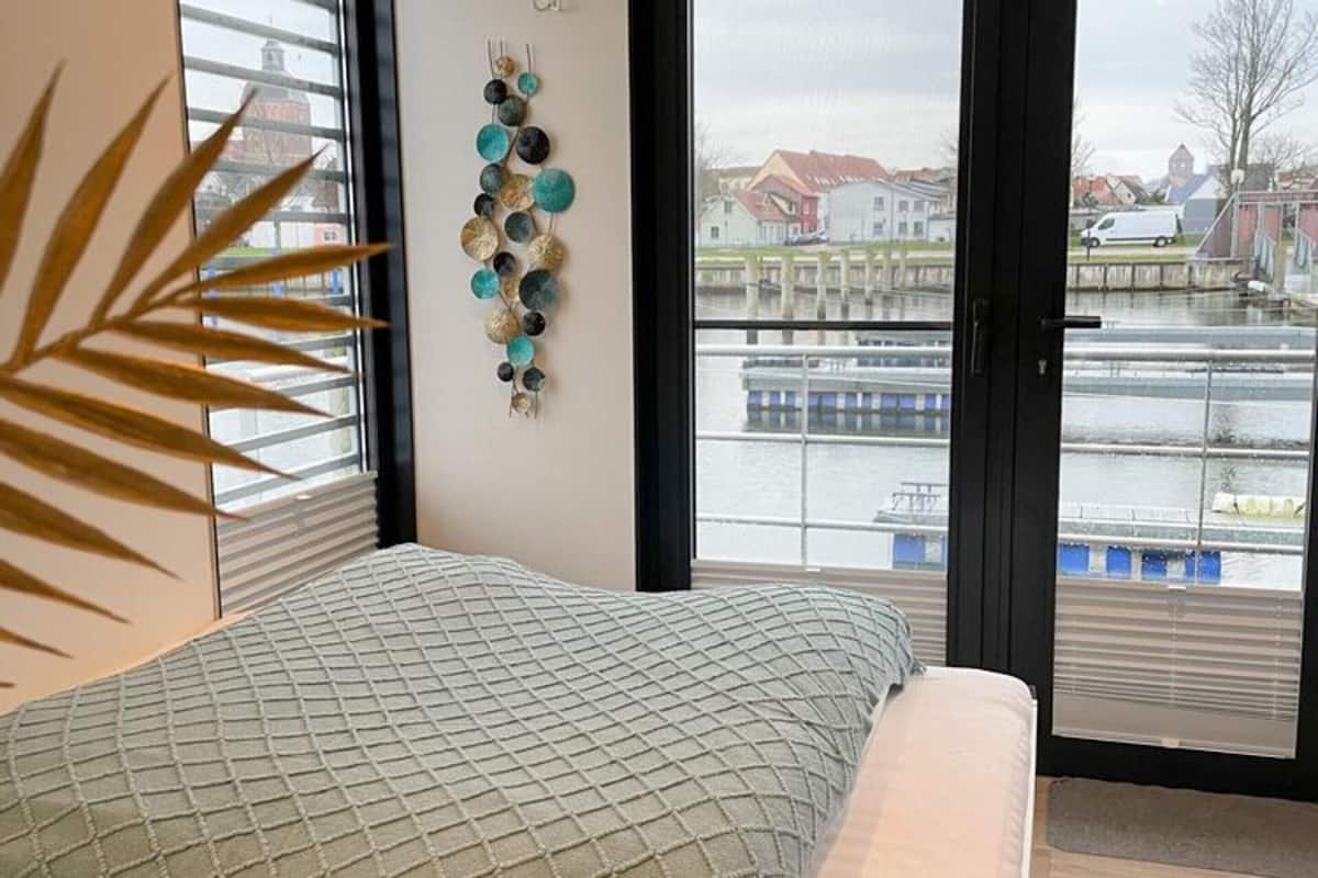 A bedroom with a bed, a window with a view of a canal and buildings, and a wall decoration.