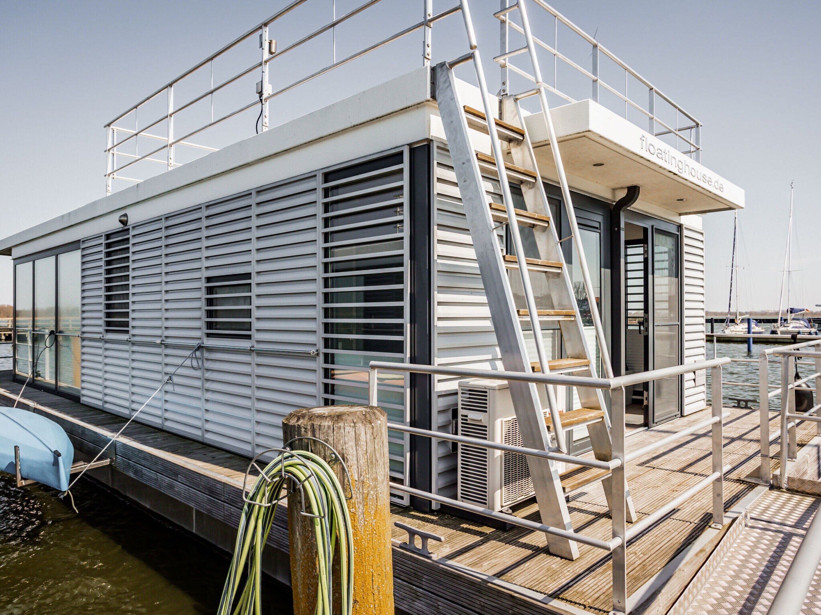A floating house with a deck, a ladder, and a railing.