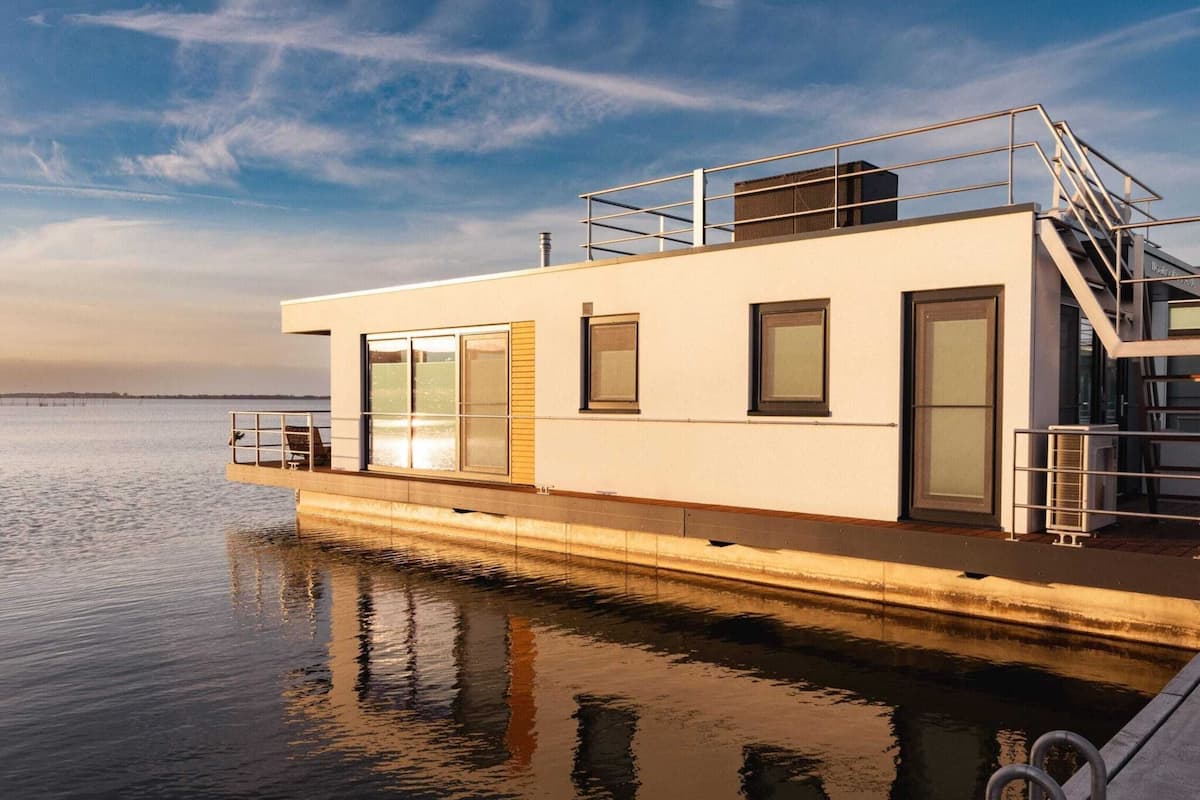 A modern, single-story boat with a flat roof, large windows, and a covered deck area.