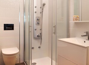 Une salle de bain moderne avec une douche à parois de verre, des toilettes et un lavabo surmonté d’un miroir.