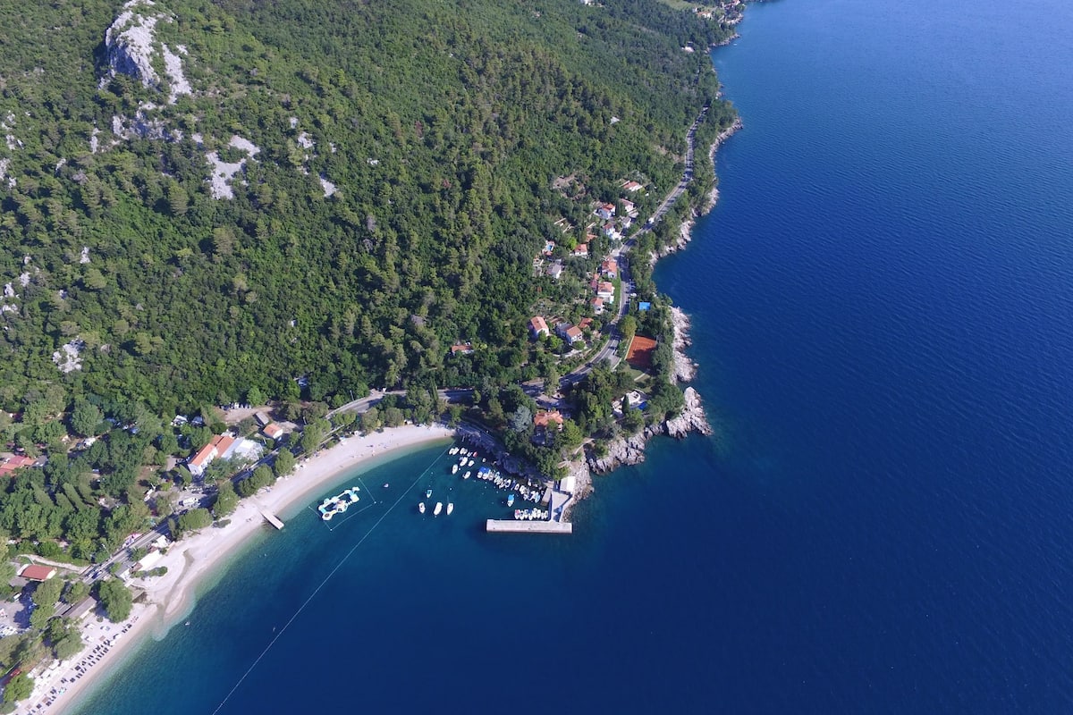 An aerial view of a coastal area with a beach, boats, and a marina.