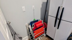 A corner of a room with a wooden floor, a white wardrobe, and a cart with red and blue bags.