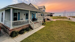 A two-story house with a porch, brick foundation, and a view of the ocean at sunset.