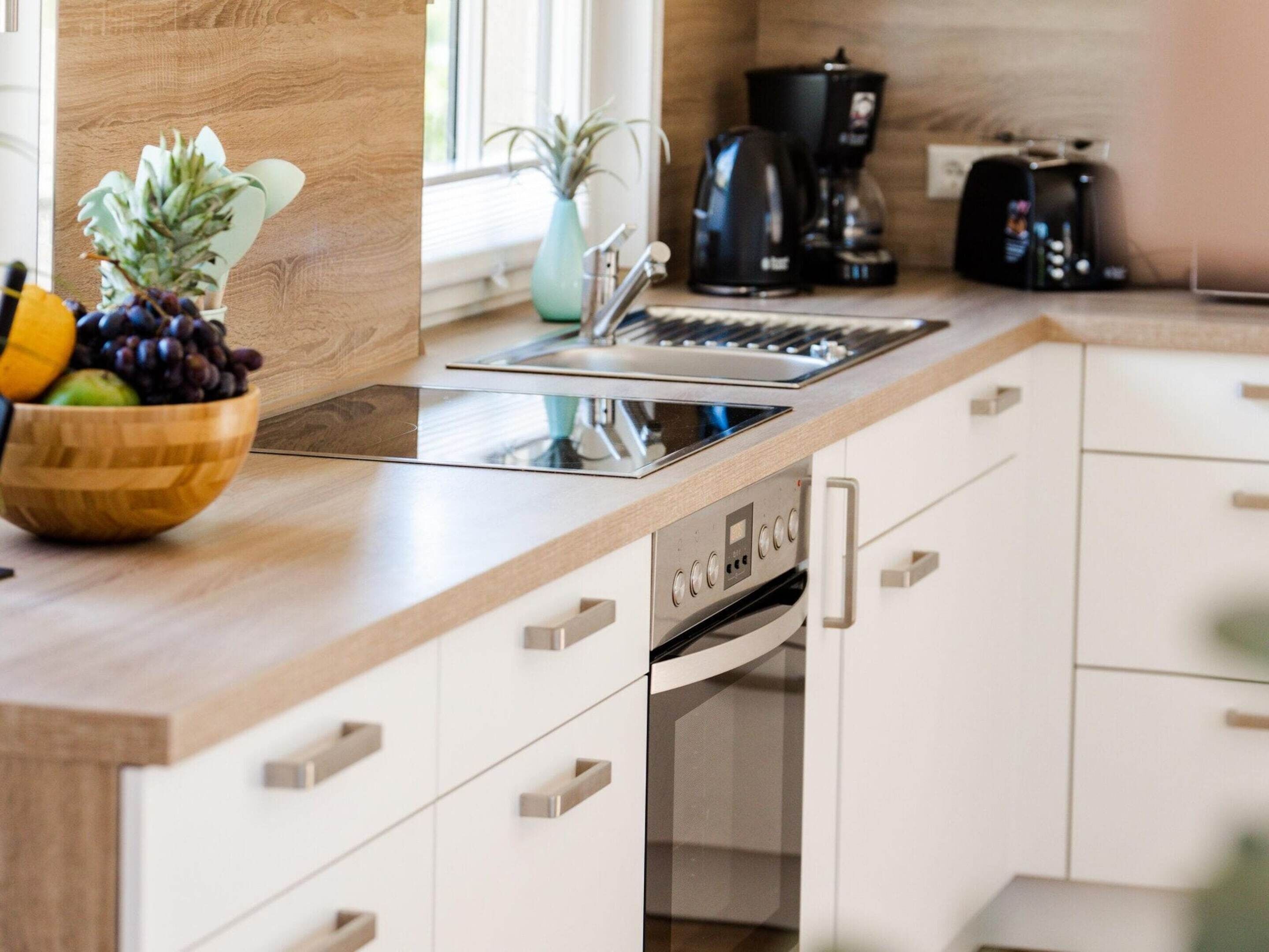 Una cocina moderna con encimera de madera, horno empotrado y cafetera.