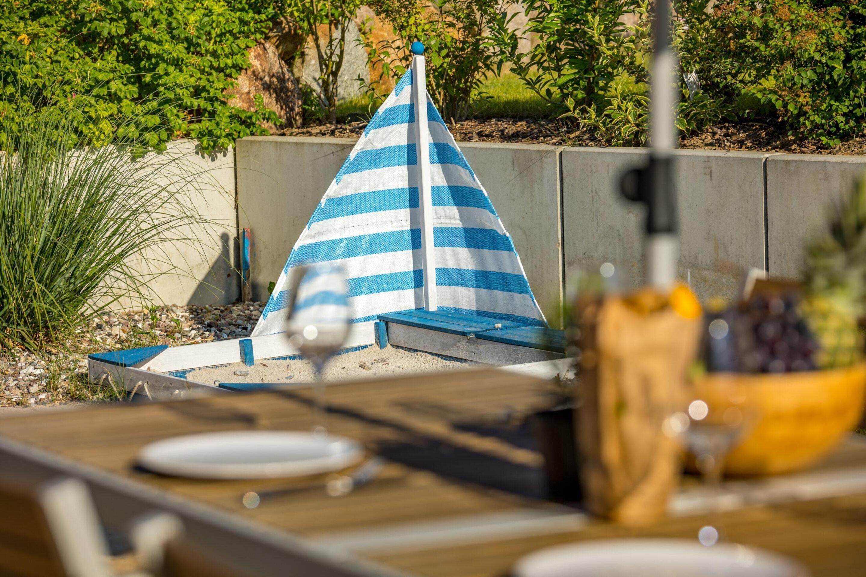 Een eettafel met een blauw-wit gestreepte parasol, een fruitschaal en een betonnen muur op de achtergrond.