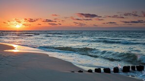 A beach with a wooden pier extending into the ocean, waves gently lapping at the shore, and the sun setting in the background. - Holiday Home With Sauna in Boiensdorf (Boiensdorf)