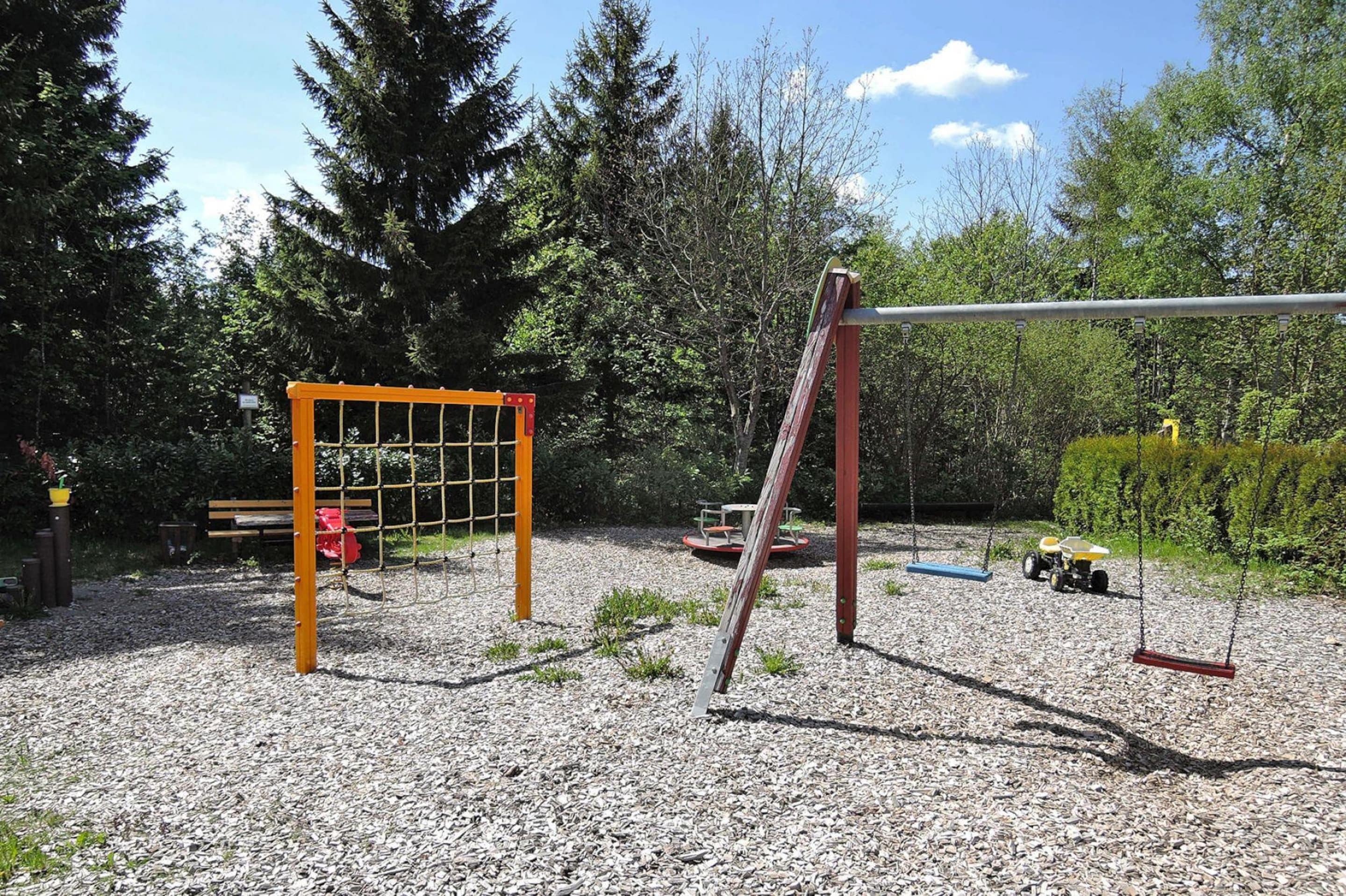 Un parque infantil con columpios, una estructura para escalar y un tractor al fondo.