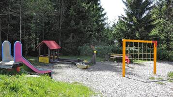 A playground with a slide, a small house, and a netted climbing structure.